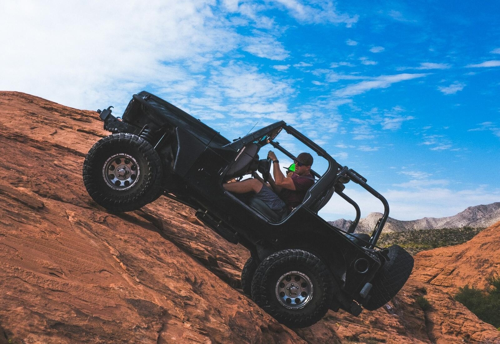 Black Jeep Wrangler climbing red rock, person inside, no top